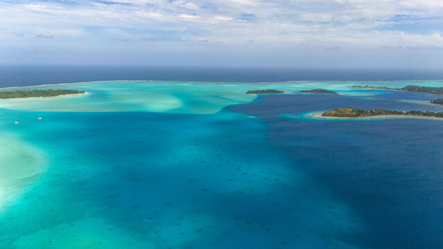 Multiple shades of blue, turquoise and azure ocean sea water surrounding the tropical island of Bora Bora. Aerial view captured by drone.  - Powered by Adobe