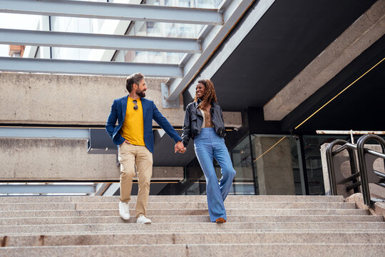 Stylish couple walking hand in hand down city stairs