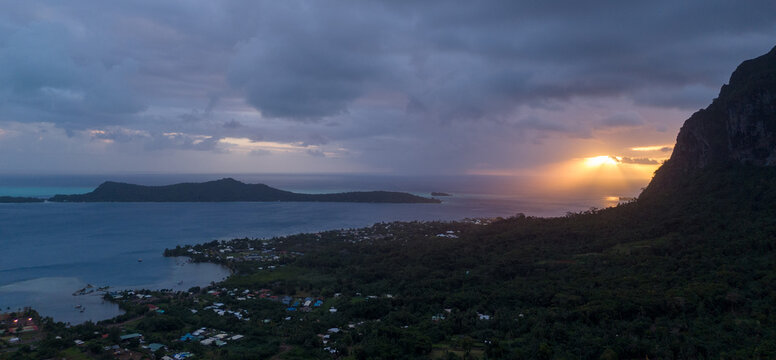 Sunset behind Mount Otemanu on the tropical island Bora Bora. The mountain is covered with low clouds in the sky. The view of ocean water is beautiful. 