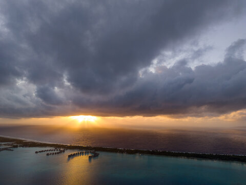 Dark storm clouds with the sun peaking out in the morning for sunrise over Bora Bora overwater bungalows or huts at an exotic Polynesian resort. 