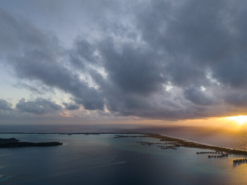 Dark storm clouds with the sun peaking out in the morning for sunrise over Bora Bora overwater bungalows or huts at an exotic Polynesian resort. 