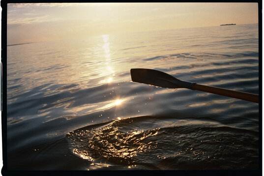 Oar Dipping Into Water at Sunset