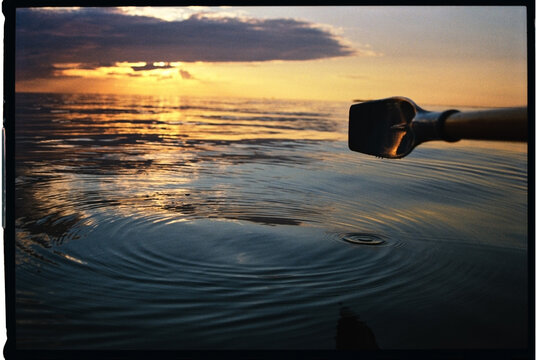 Oar Dipping Into Water at Sunset