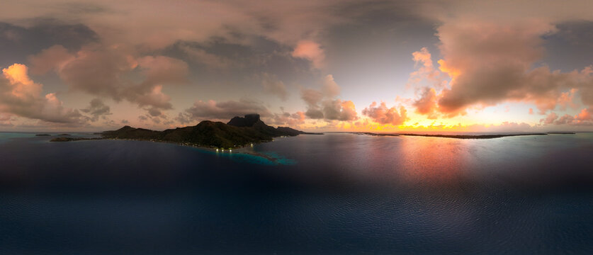 Sunrise over  tropical island Bora Bora in French Polynesia. Low clouds float above the extinct volcano on the popular tourist destination in the south pacific sea. Aerial drone view of paradise. 