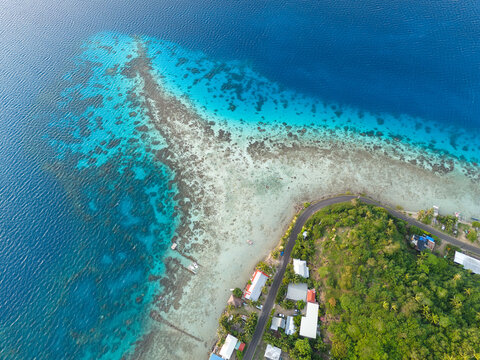 Aerial view captured by drone over clear azure South Pacific Ocean water off the coast of tropical island Bora Bora in French Polynesia. Vibrant coral reefs can be seen in colorful blue turquoise. 