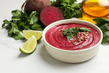Tasty beetroot hummus in bowl and products on white marble table
