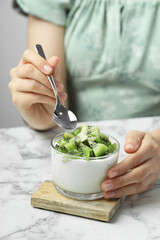 Woman eating tasty yogurt with fresh kiwi at white marble table, closeup