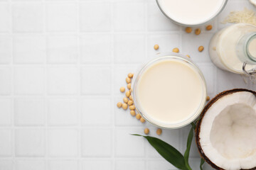 Different types of vegan milk and ingredients on white tiled table, flat lay. Space for text