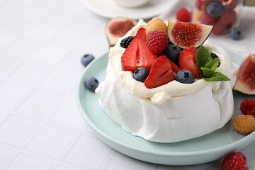 Pavlova cake (meringue dessert) with whipped cream, fresh berries, mint and fig on white tiled table, closeup