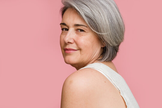 mature woman with grey hair posing on pink background