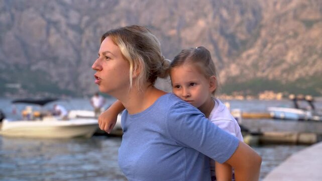 Mother and little daughter spending time together on the vacation, piggyback ride by the sea shore 