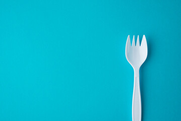 Flat lay of white plastic spork (fork plus spoon) on blue background with copy space. Abstract...