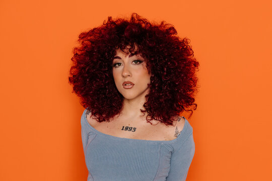 Woman with voluminous curly red hair against vibrant orange background