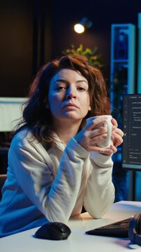 Vertical video Portrait of happy computer engineer enjoying hot tea while implementing security measures to protect company systems and data. Joyful IT worker holding coffee mug and debugging code