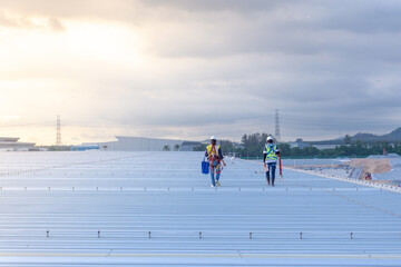 Two engineers wearing full safety body harness working inspection on Metal roof top of large warehouse  © Kittisak