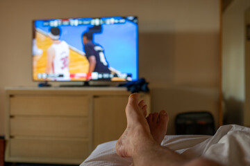 Selective focus on propped up feet with a blurred basketball game on the TV