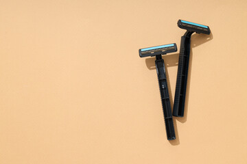 Two men's black disposable razors on beige background, space for text