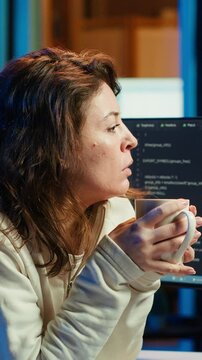Vertical video Portrait of engineer drinking coffee in the morning and futureproofing company network from downtimes. IT admin enjoying hot beverage while increasing data security, camera A