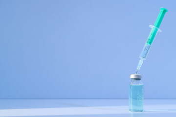 Glass medical bottle with vaccine and syringe on light background, space for text