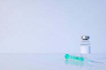 Glass medical bottle with vaccine and syringe on light background, space for text