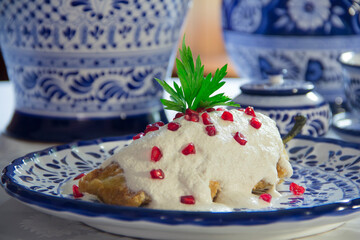 Authentic mexican Chiles en Nogada, roasted and stuffed poblano pepper with walnut white sauce and fresh pomegranate, served over talavera plate at Puebla city, Mexico.