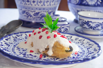 Chile en Nogada, roasted and stuffed poblano pepper with pecans white sauce and fresh pomegranate, served over talavera plate.