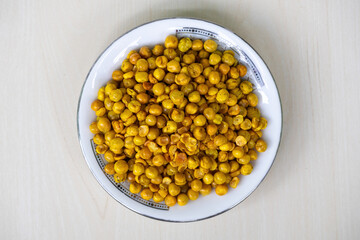 Spicy fried peas on white plate on wooden surface. Delicious snack food also known as dabli boot bhaja, spicy green peas, masala matar, hara matar, masala vatana, chatpata matar vaja. Top view.
