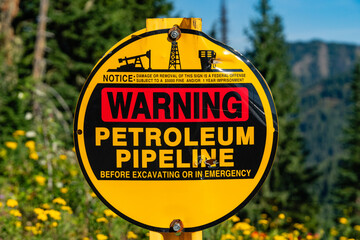 Close-up of bright yellow sign warning that a petroleum pipeline is buried here. In background are...