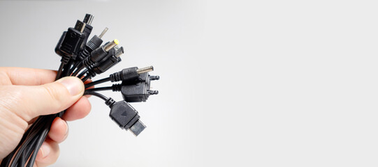 many cords with different types of connectors for charging phones on a gray background with empty...