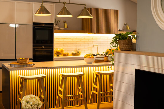 Modern kitchen with illuminated island, wooden stools, and stylish decor elements, copy space