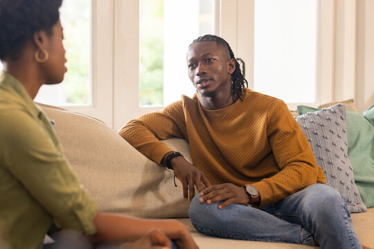 African American couple sitting on couch, having serious conversation in living room at home