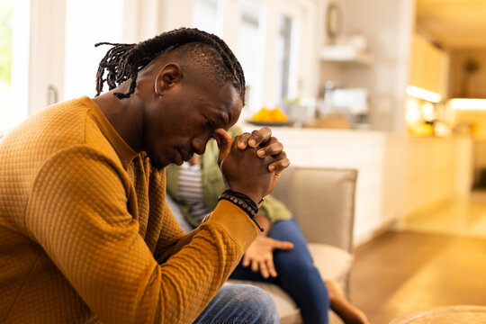 African American couple sitting on couch, deep in thought, hands clasped together in living room