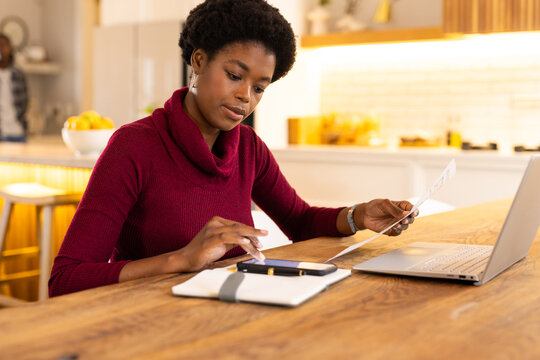 Paying bills online, African American woman using smartphone and laptop at home