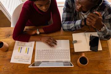 Analyzing financial documents, African American couple working with laptop and notepad at home