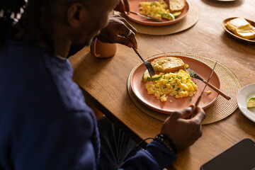 Eating breakfast, African American man enjoying scrambled eggs and toast at dining table