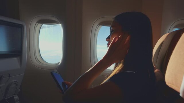 Asian woman using headphone listen to music while sitting in airplane. 
