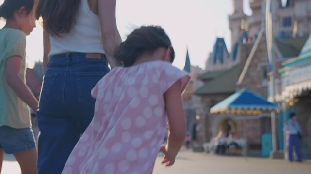 Asian mother and adorable kid daughters walking at the theme park. 