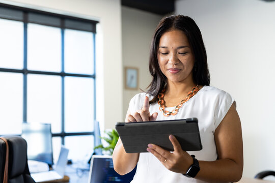 Using tablet, businesswoman working in modern office with large windows