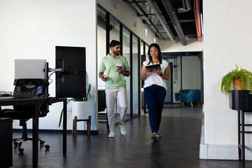 Walking in office, colleagues discussing work while holding tablet and coffee cup