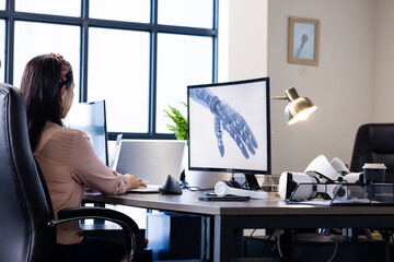 Working in office, woman using laptop and desktop with robotic hand image
