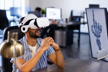 Using VR headset, Indian man interacting with robotic hand design on computer screen