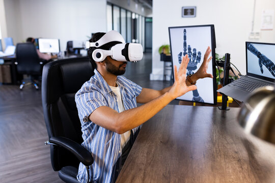 Using VR headset, Indian man interacting with robotic hand simulation in modern office
