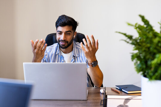 Using laptop, Indian man discussing work in virtual meeting at office desk