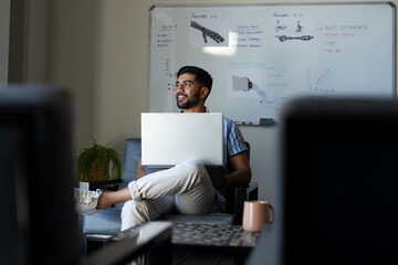 Holding laptop, Indian man smiling and working in modern robotic office