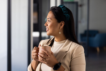Holding coffee mug, woman smiling and looking out window in office