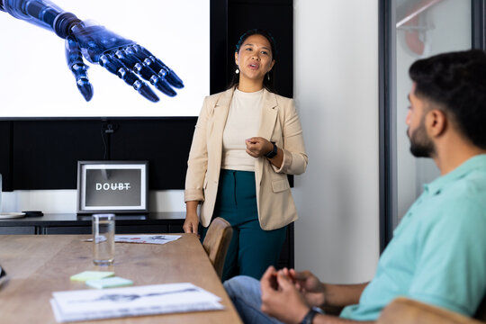 Presenting in office, woman discussing robotic arm with colleague during meeting