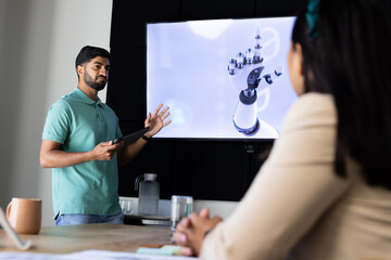 Presenting robotic hand design, Indian man using tablet in modern office meeting