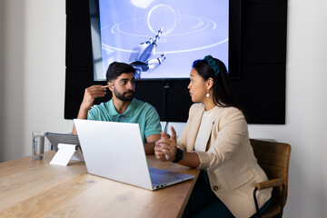 Discussing robotics, colleagues using laptop and tablet in modern office setting