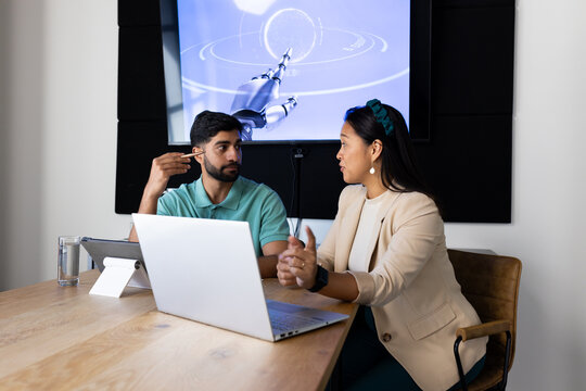 Discussing robotics, colleagues using laptop and tablet in modern office setting