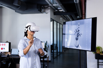 Using VR headset, woman interacting with virtual robotic hand in office